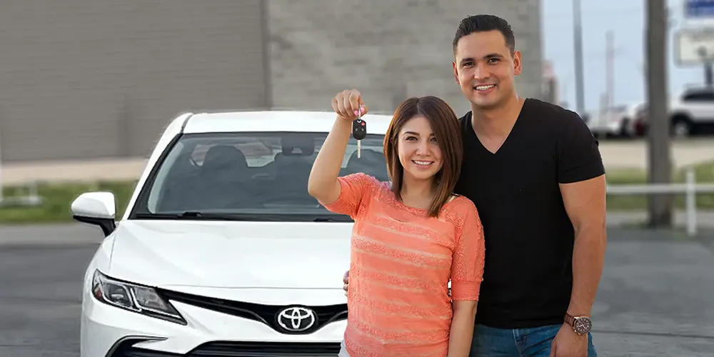 happy couple holding keys in front of their new used car